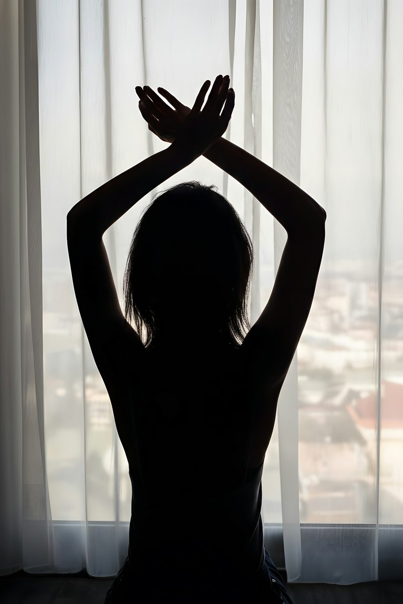 Silhouette vue de dos, bras croisés au-dessus de la tête devant une fenêtre voilée
