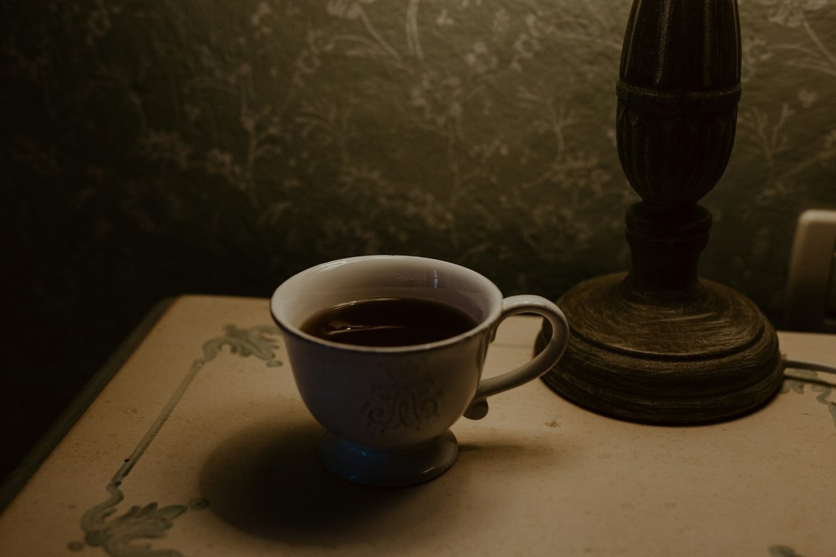 Tasse de boisson chaude posée sur une table près du pied d'une lampe, lumière du soir