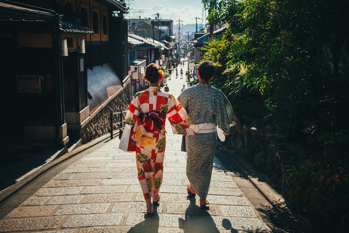 Deux personnes en yukata, vues de dos, marchant dans une rue pavée bordée de maisons de bois